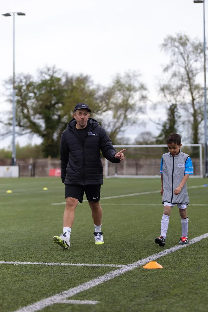 EPP coach directing young athlete through movement drill on pitch Birmingham